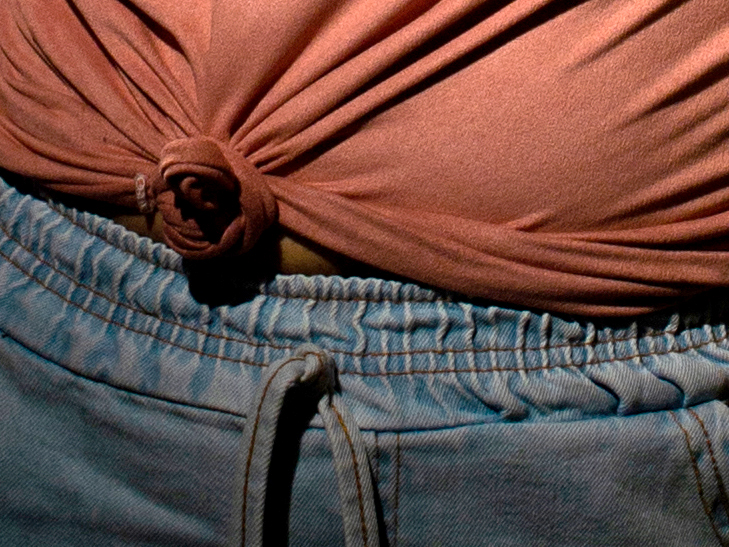  Foto do detalhe do nó na blusa rosa e o cos de uma calça jeans. Logo abaixo o vídeo com acessibilidade em Libras.