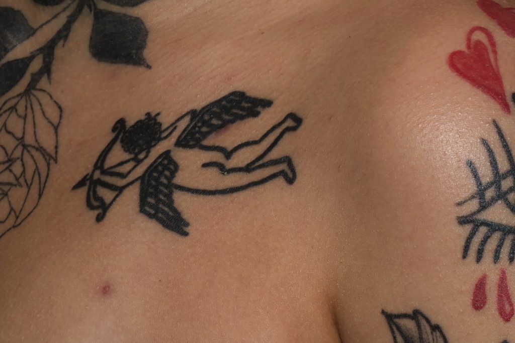 Detalhe de tatuagem no ombro, um flores, cupido flechando, um coração vermelho